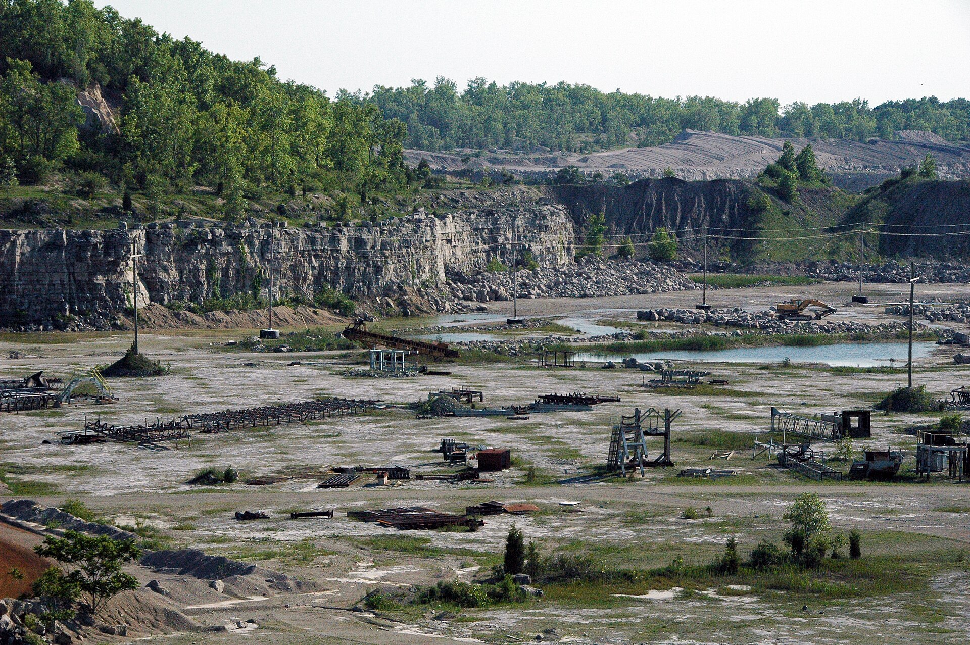 Wide view of a limestone quarry rock face with excavation equipment on the quarry floor